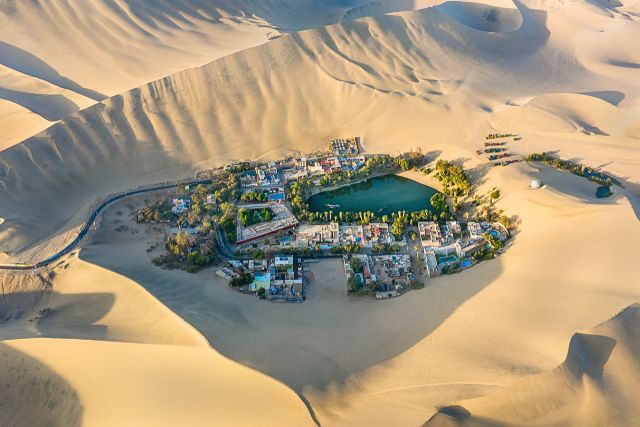 Vista aérea del oasis de Huacachina y su laguna verde rodeada de enormes dunas de arena cerca de Ica, Perú