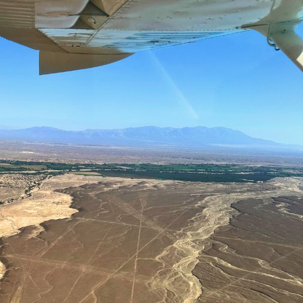 View from under the wing of a small aircraft over the Nazca desert, with lines crossing the plain