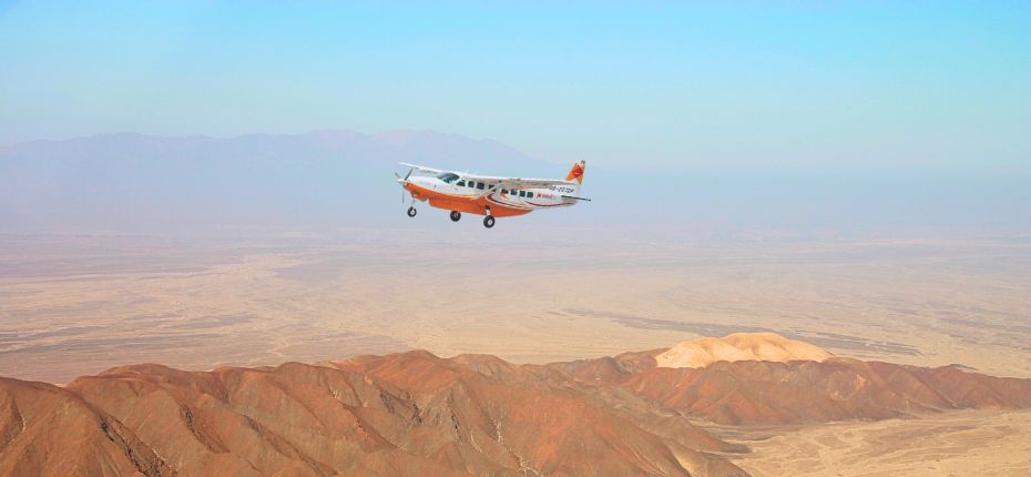 Cessna Grand Caravan flying over red desert mountains under a clear sky on the way to the Nazca Lines