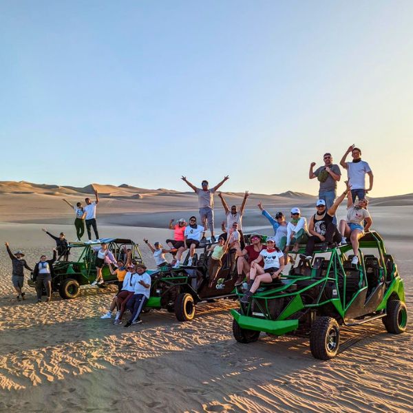 Dune buggy stop in the Huacachina desert Group of travelers cheering beside green dune buggies on the sand dunes of Huacachina