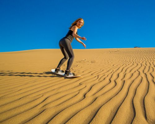 Sandboarding on the Ica dunes Woman sandboarding standing up on a golden dune under a clear blue sky near Huacachina