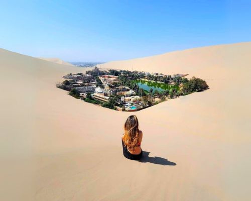 View over the Huacachina oasis Traveler sitting on the top of a dune looking down at the Huacachina oasis and lagoon
